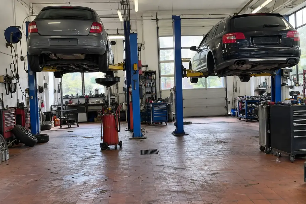Werkstatthalle mit Fliesenboden, zwei blauen Hebebühnen mit angehobenen Autos, Werkzeugwagen und Ölauffanggerät