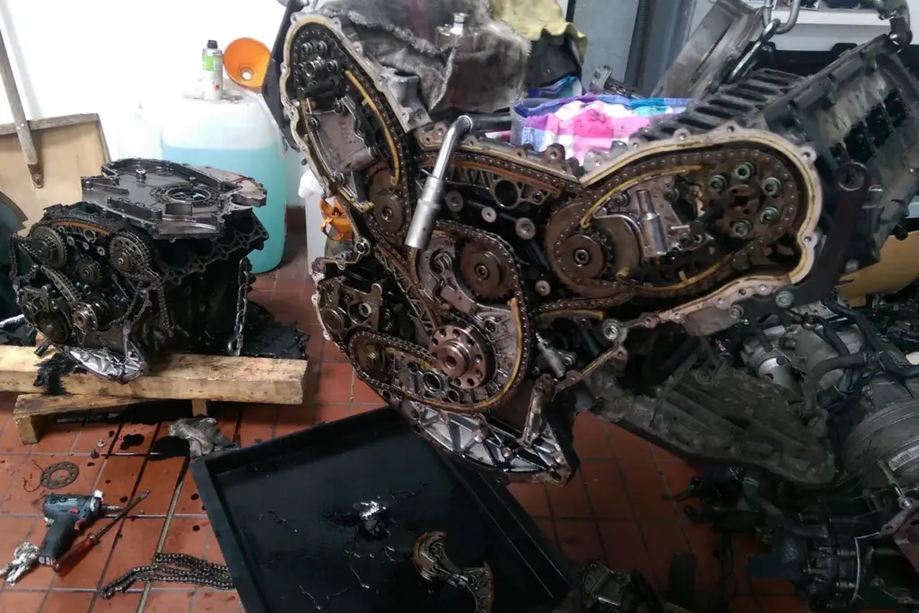 Ausgebauter V8-Motor eines Audi A8 mit geöffnetem Steuertrieb: mehrere Steuerketten, Kettenräder und Gleitschienen, daneben ein zweiter Motorblock auf Holzklötzen